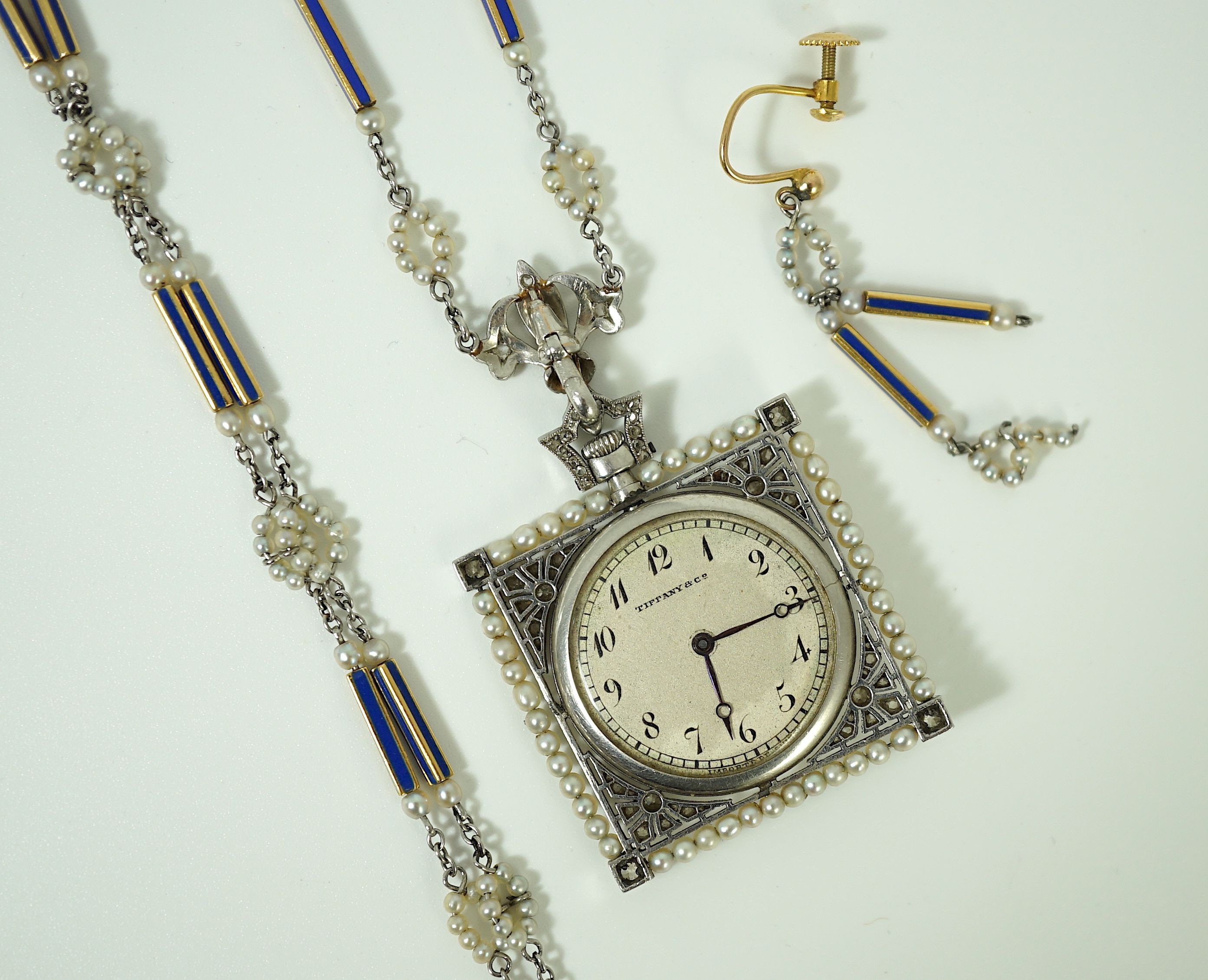 An early 20th century Tiffany & Co platinum, seed pearl and diamond set pendant square open faced dress timepiece, on a platinum, gold, enamel and seed pearl set chain, together with a matching 9ct bracelet and 9ct earri